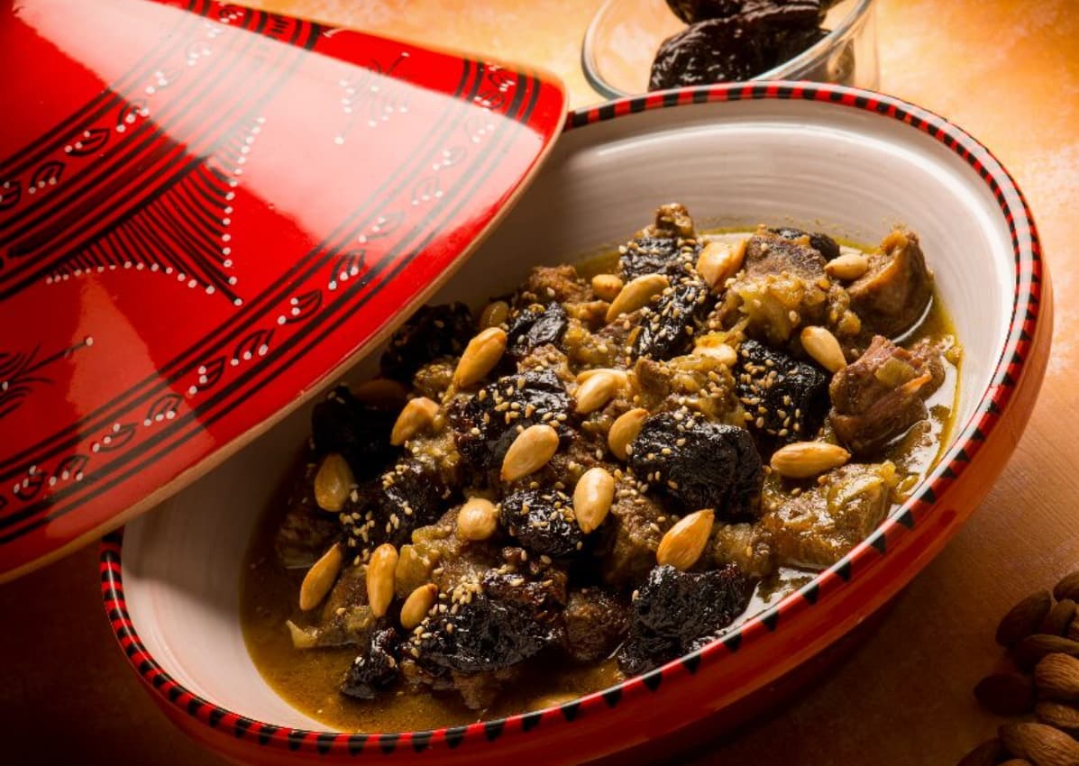 Moroccan lamb tagine with prunes, almonds, and sesame in a red ceramic tagine